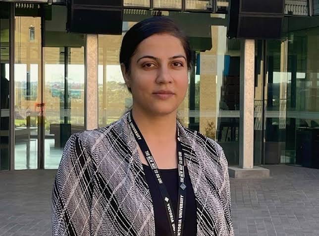 A young woman in professional dress and work lanyard poses in a courtyard