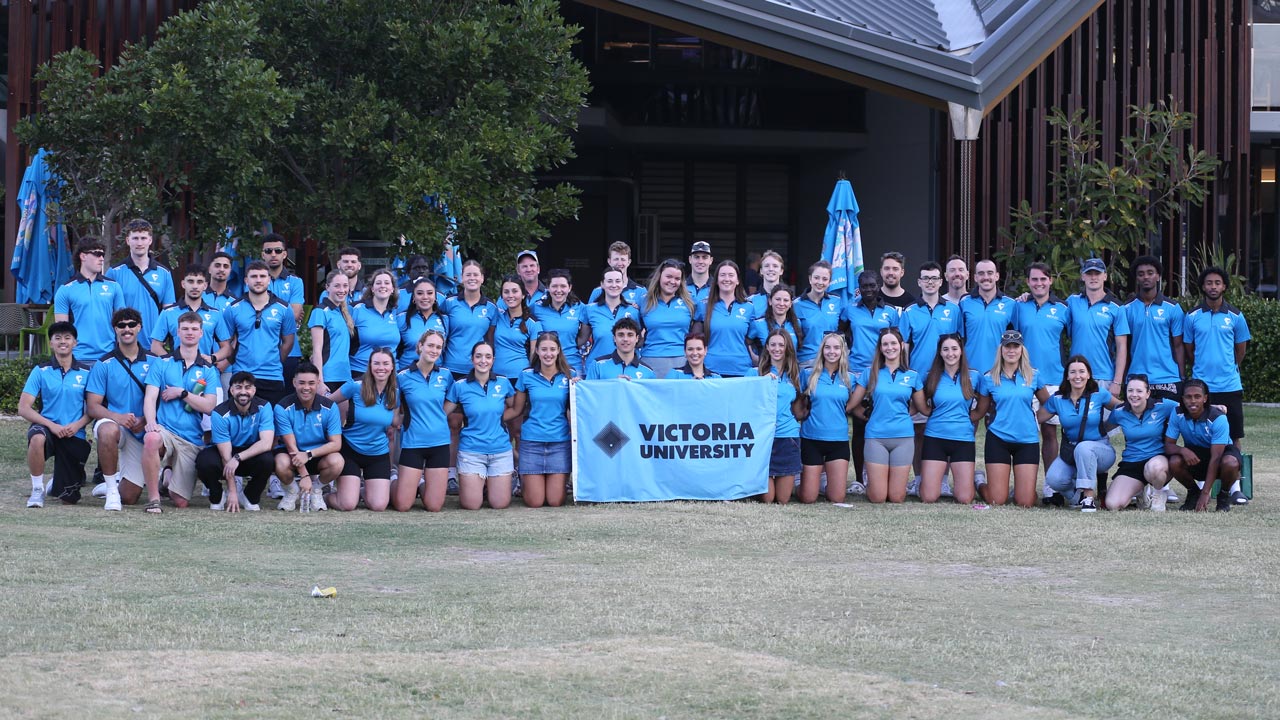 A group photo with a large number of VU Vultures team members, standing behind a Victoria University sign.