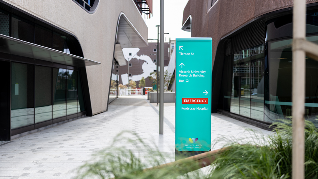 A courtyard between two modern buildings with a hospital sign indicating Footscray Hospital and Victoria University research facilities 
