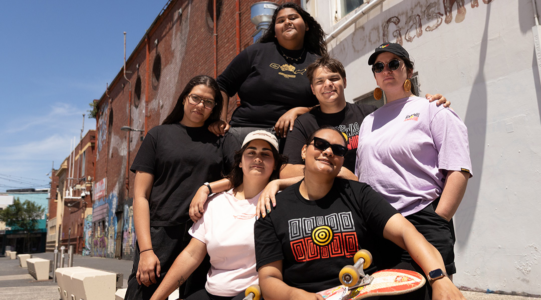 Smiling group of students in the sun wearing t-shirts with first nations graphics.