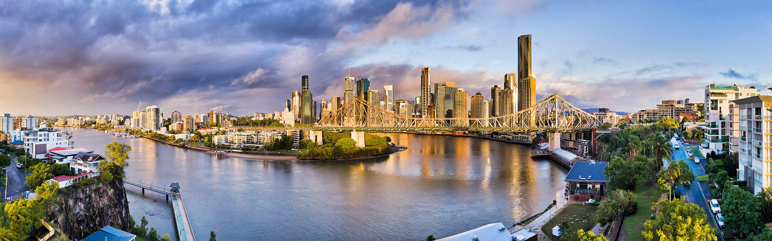 View of Brisbane, Australia city skyline and river with sunshine and dramatic clouds.