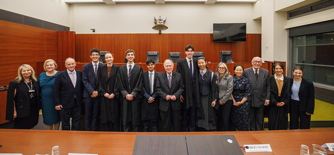 A group of young and older adults in formal and legal dress pose in a court room
