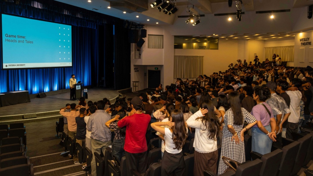 Students stand and participate in an interactive game inside a theatre during an orientation session.