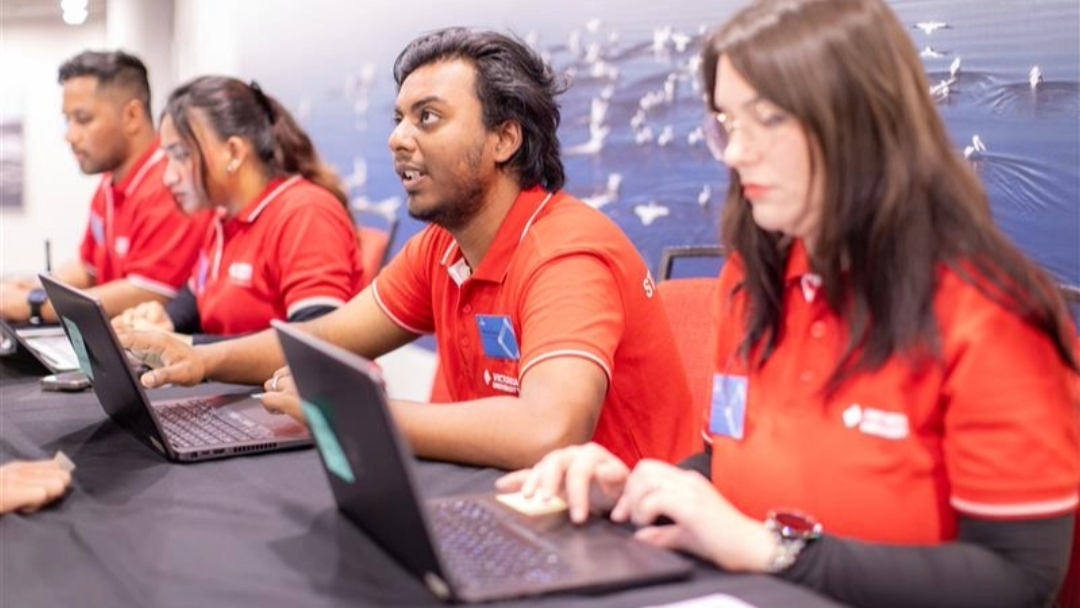 Student mentors sit at a registration desk using laptops to assist students during orientation check-in.