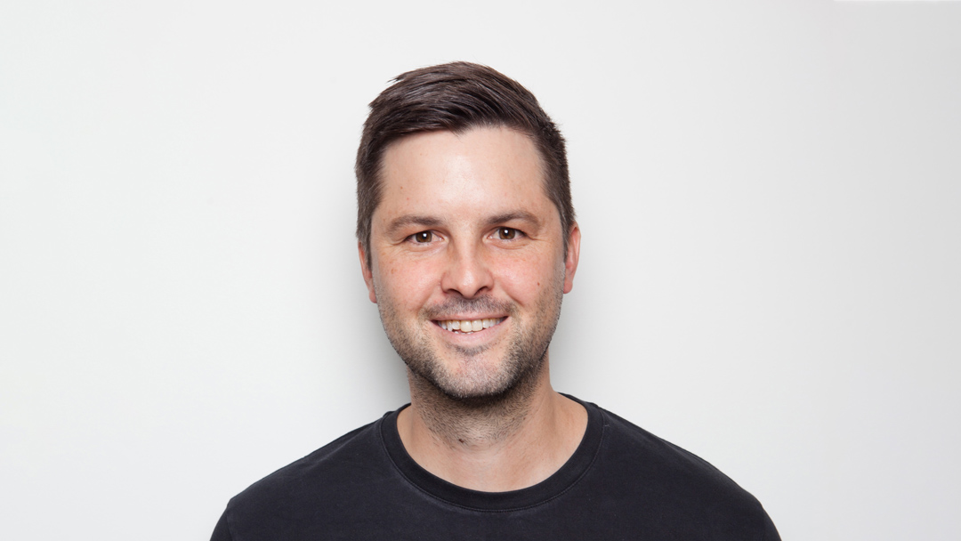 Smiling headshot of man in black t-shirt.  