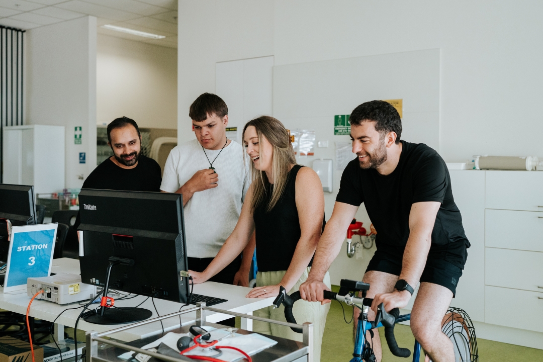 Exercise physiology students stand around computer and stationary bike