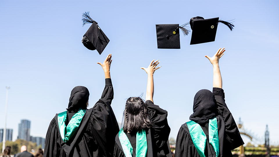 Three graduates throw their caps in the air joyously after their graduation ceremony