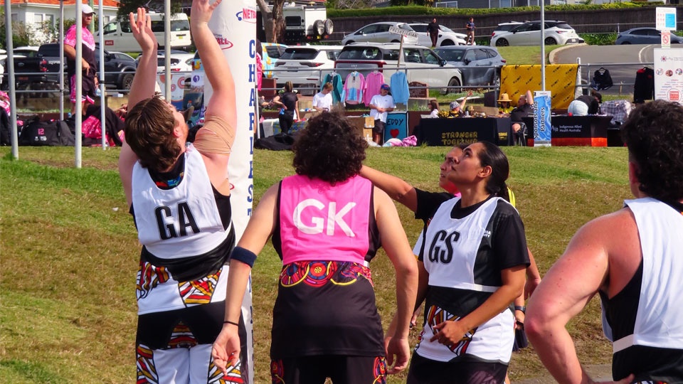 An action shot of the team playing netball. Goal attack shoots for goal while the other players in the ring await the goal or rebound.