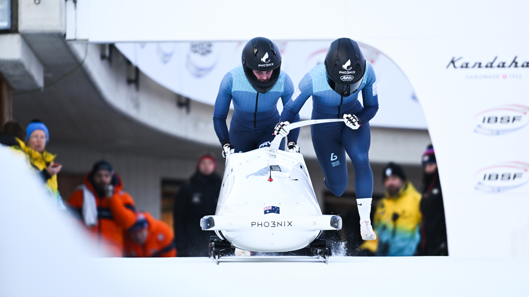 A two-person bobsleigh team taking off in full gear and helmets