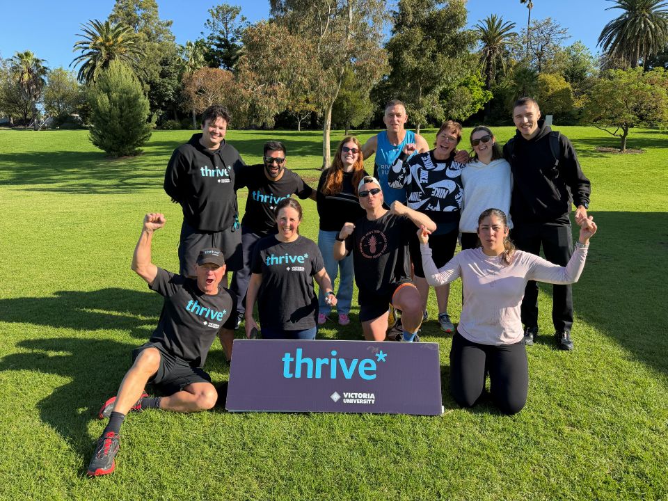 A group of runners posing in a park behind a sign that says thrive*.
