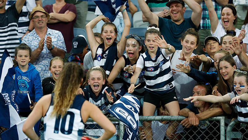 crowd including young girls in footy uniforms cheering
