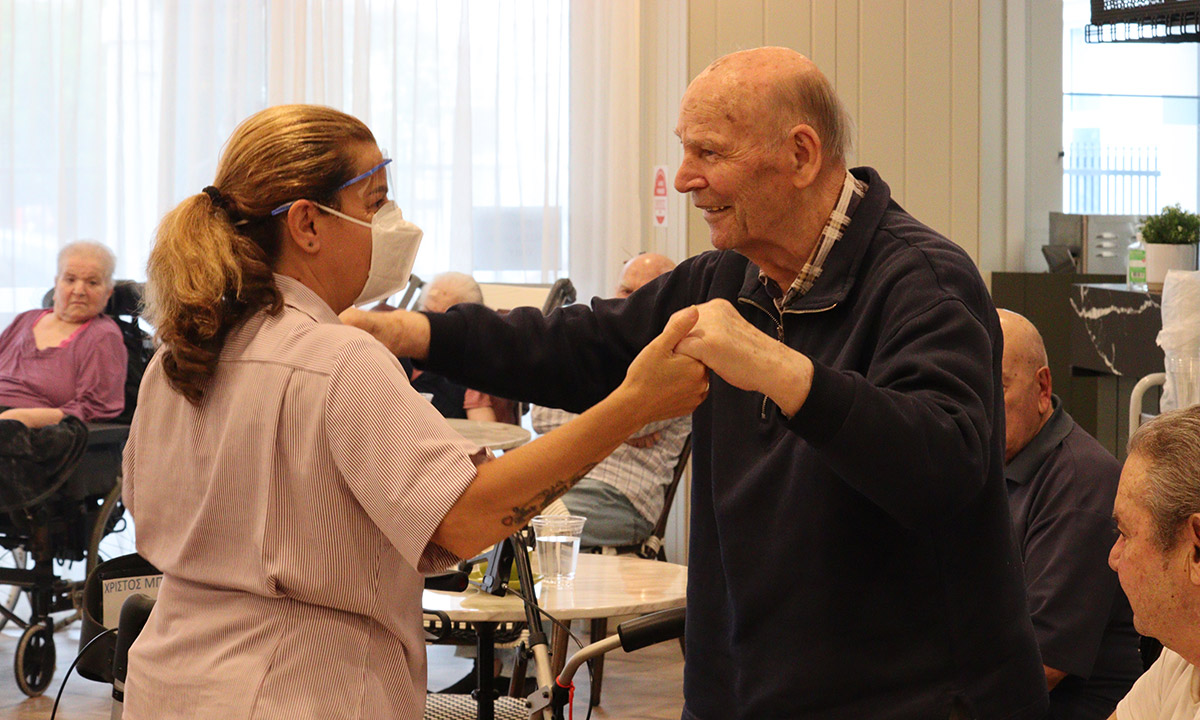 An elderly man dances with a carer