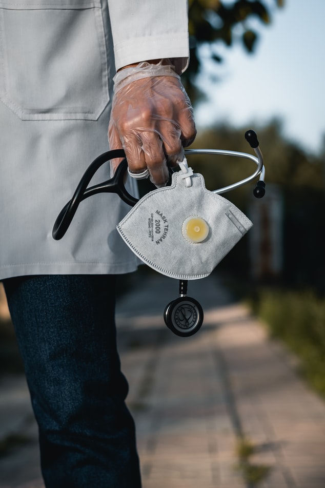 A gloved hand holding a mask and stethoscope
