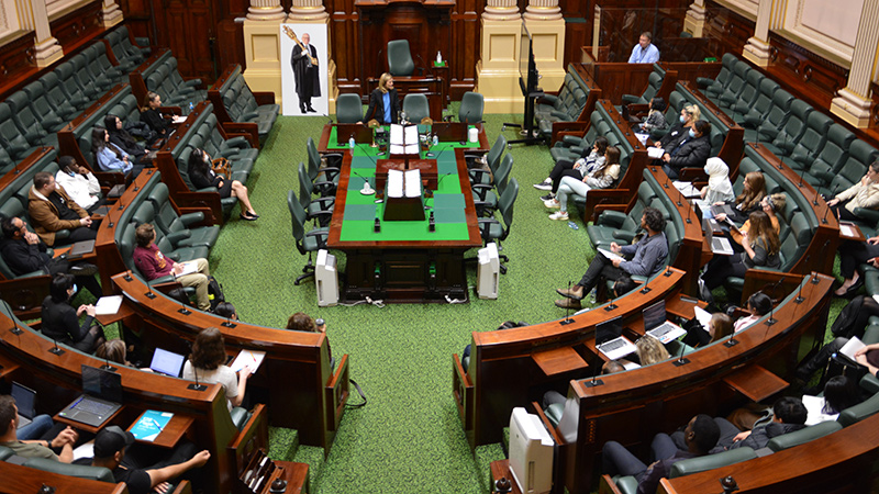 A stately looking room from above with curved wooden seating, with young people in seats