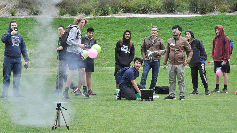 Young men watch a smoking mini launch pad