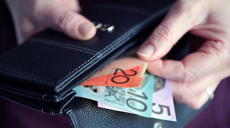 A hand pulling a $20, $10 and $5 note out of a wallet.