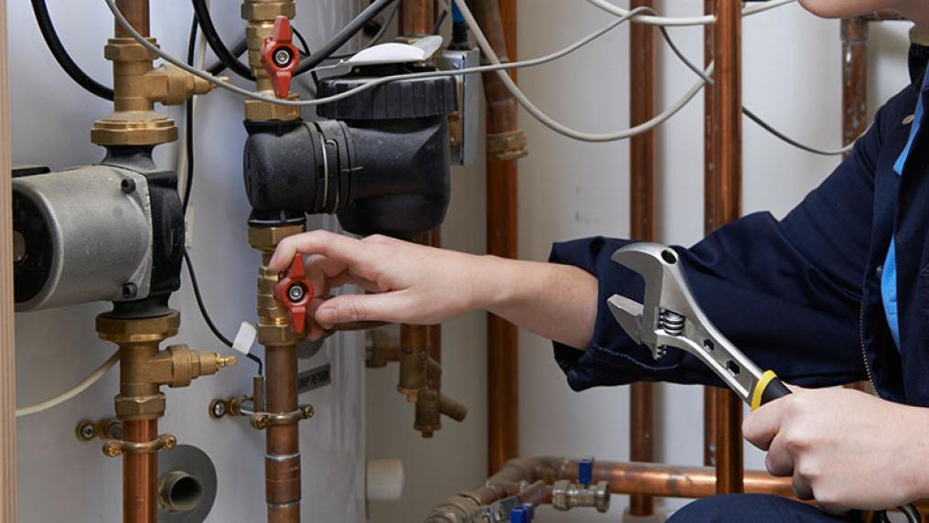 Close up of hands of a female plumber fixing pipes with a spanner.
