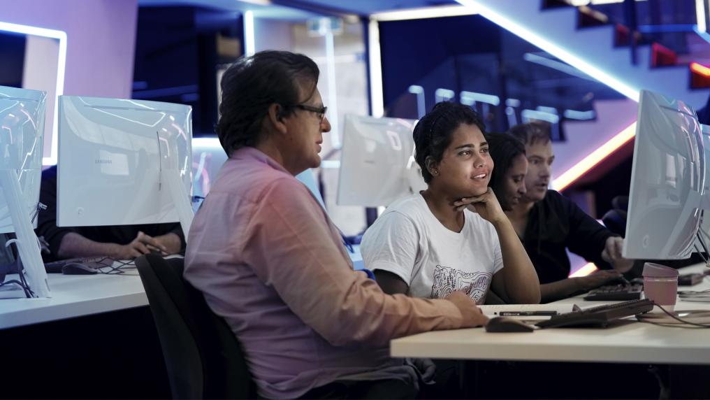 A student and a teacher sitting in a computer lab looking at a computer.