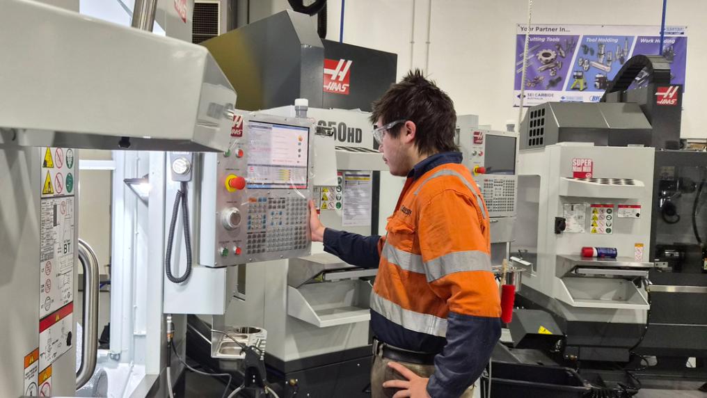 A student wearing high visibility clothing and protective goggles is using a modern manufacturing machine.
