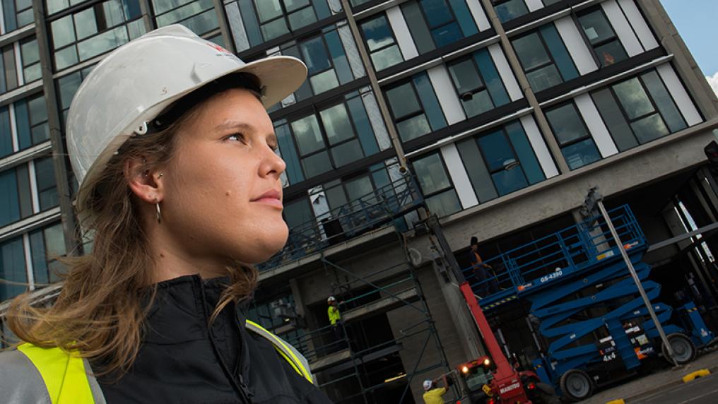 Emma Buis, engineering alumni, standing in front of skyscraper wearing construction hat.