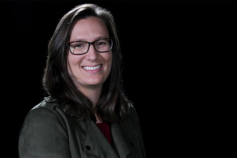 A woman wearing glasses smiles at the camera