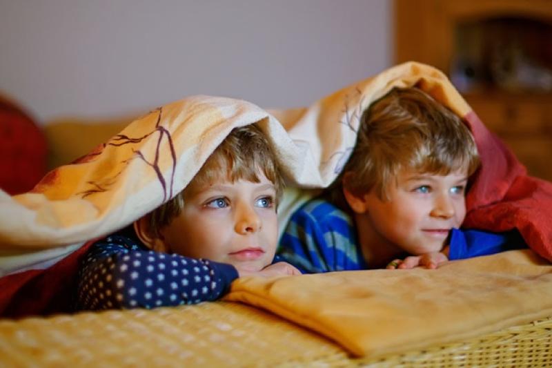 Two kids hide under a doona watching TV.