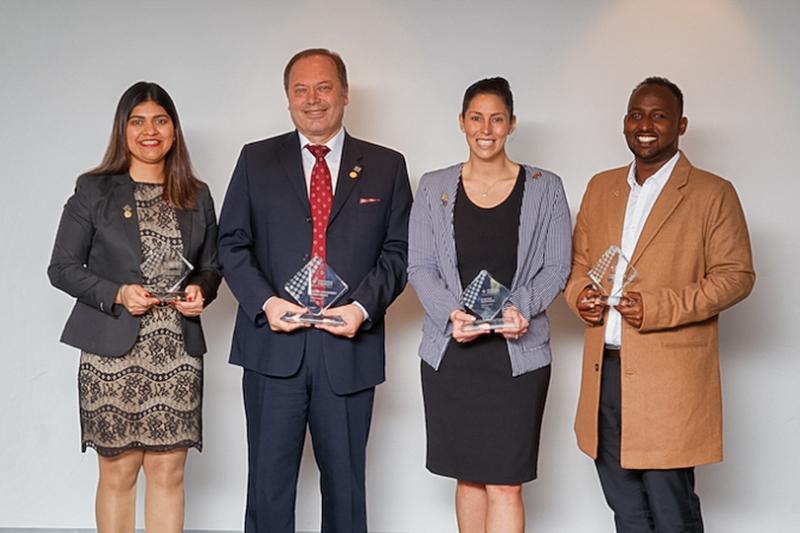 A multicultural group of men and women, in their 30s–50s, hold glass awards
