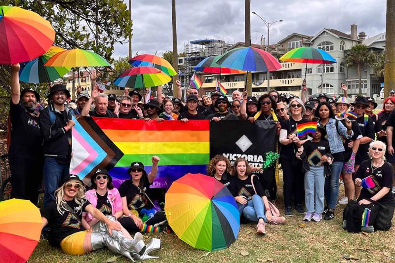 VU staff and students gather together at Pride March, holding the Pride flag and rainbow umbrellas. 