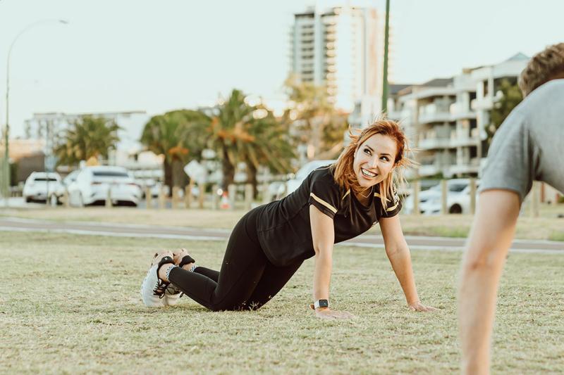 A woman doing push ups on grass outside.