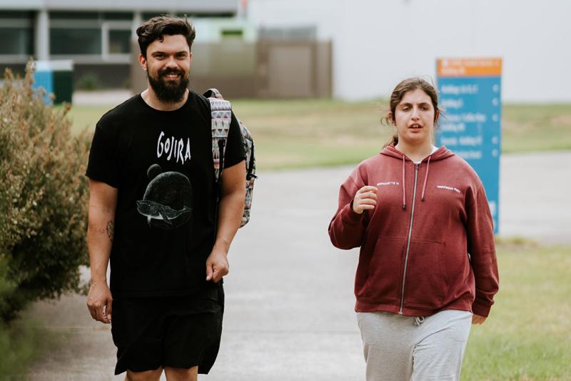 A young man walks outside with a woman who appears to have disability