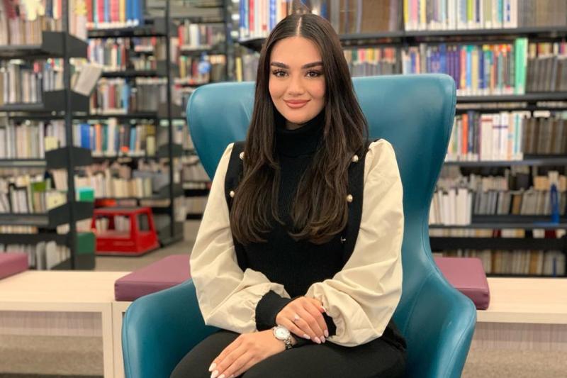 A young woman poses in front of a library bookshelf