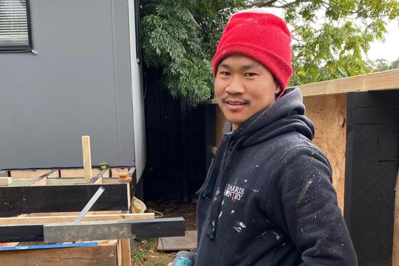 Khamh on a job site, drill in hand as he pauses to pose happily