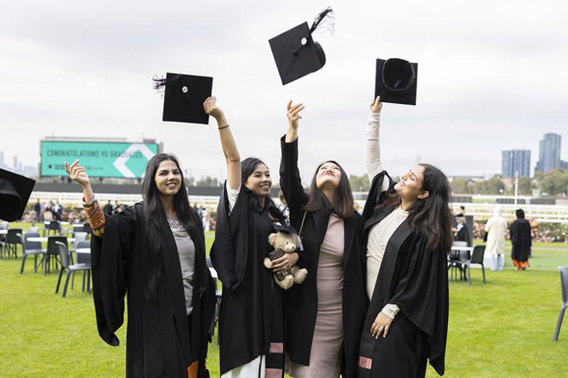 A group of four graduates throw their hats in the air.