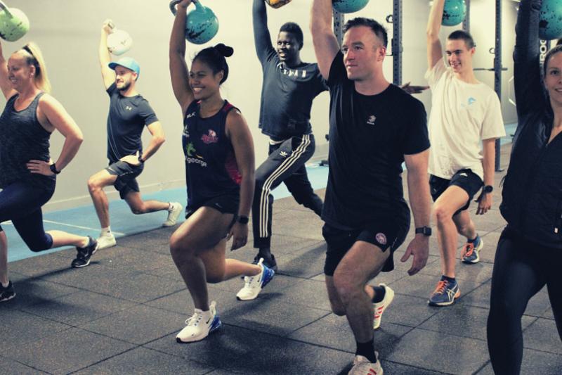 A group of people doing the same squatting exercise in a gym.