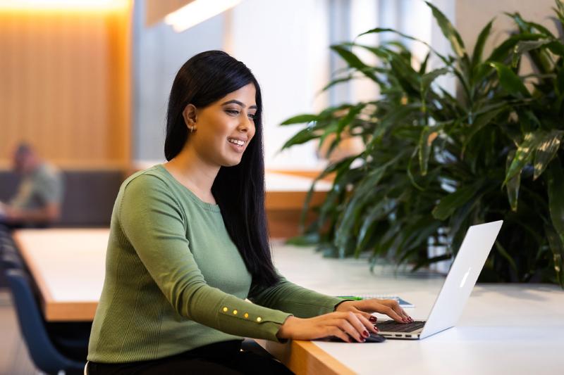 A student sits at a bench on a laptop.