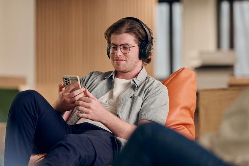 A student sits on a bean bag, with headphones on, holding a mobile phone.