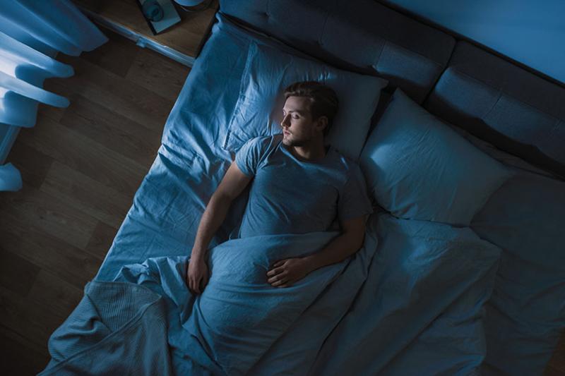 A man sleeping solo in a bed at night.