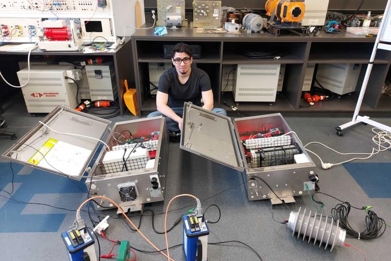 A man sits on the floor of a lab surrounded by electronic gear