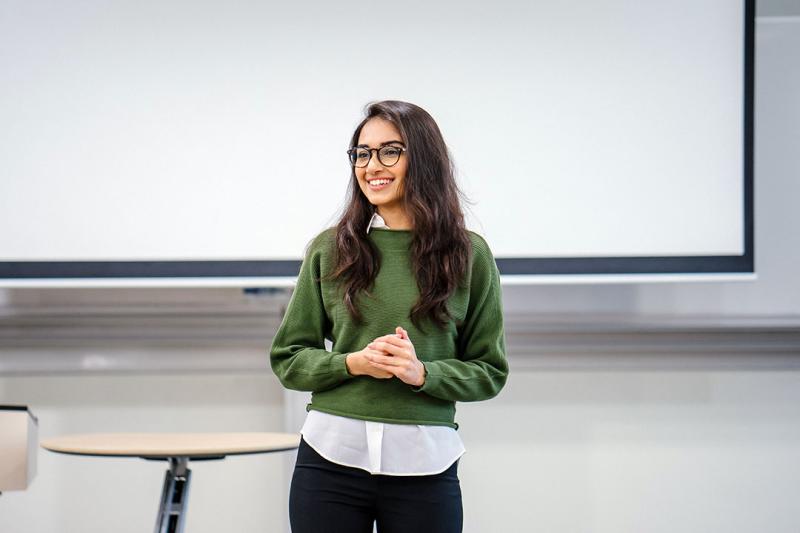 A student in glasses giving a presentation in a classroom.