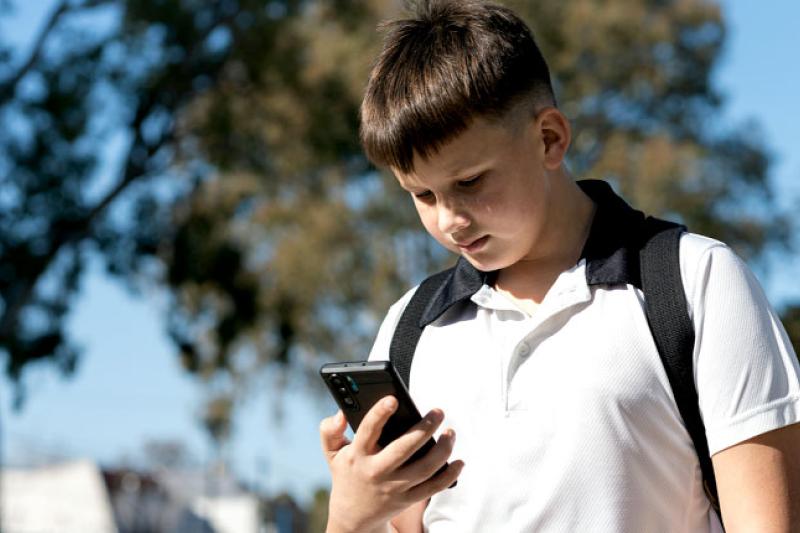 Teenage boy standing outside, holding and looking at his phone, with a concerned expression on his face.