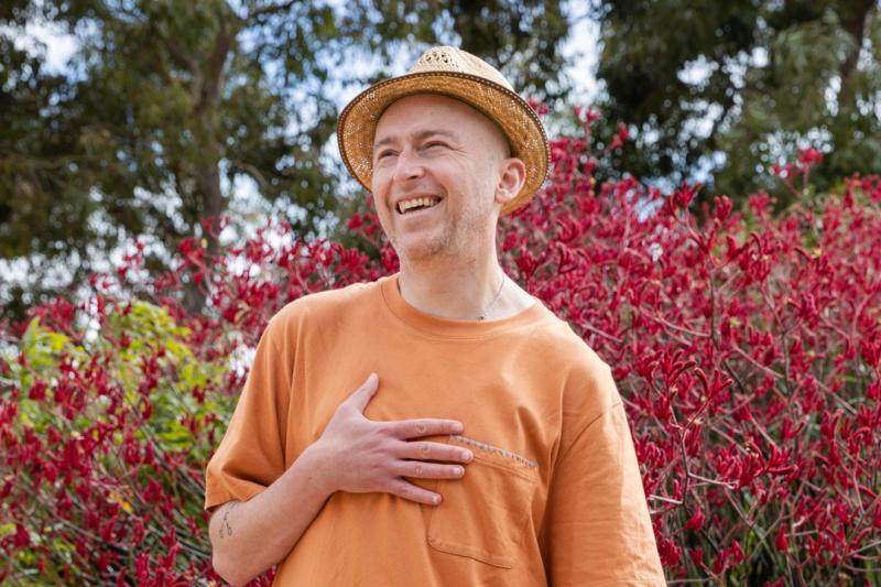 Author Joe Cranbourne standing outside in front of a flowering red bush.