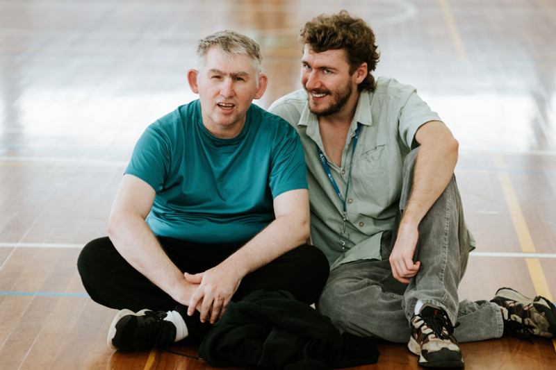 Two students at VU Aspect St Albans. The students are sitting on the gymnasium floor and smiling at the camera.