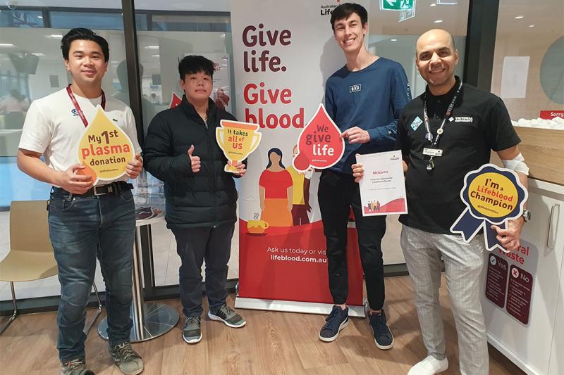 Four VU representatives stand holding signs at the blood donation clinic.