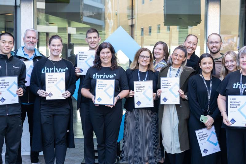 Thirteen representatives from the Thrive team smile at the camera, holding their awards for the Innovation category.