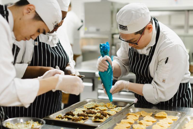 Student chefs preparing a dish. One is squeezing a piping bag.