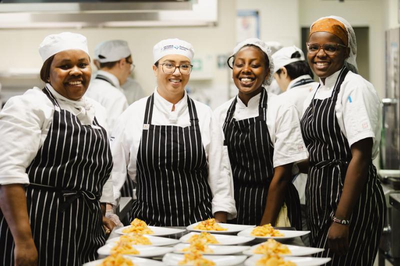 VU student chefs standing behind a set of prepared dishes, smiling at the camera