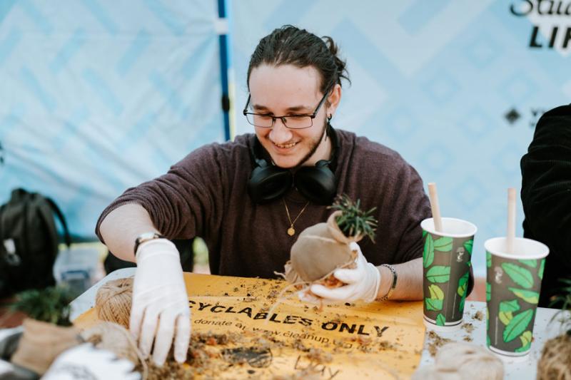 A student holding a small plant pot in one hand while grabbing dirt with their other hand.