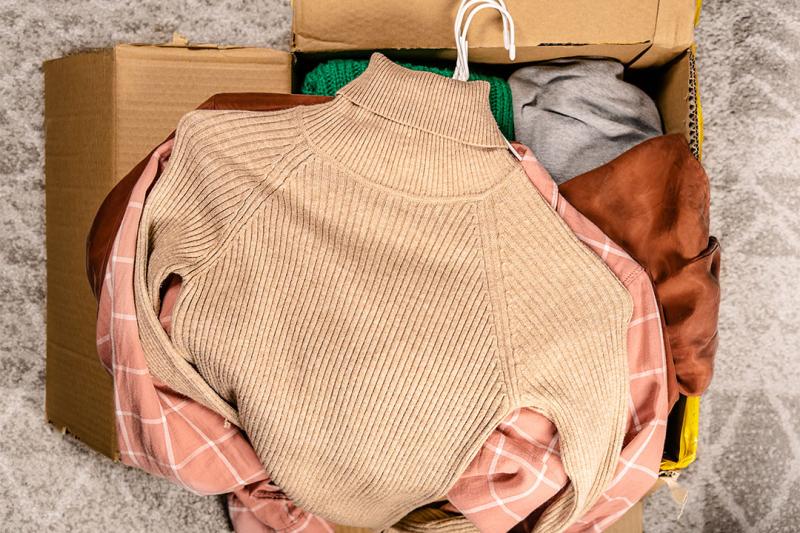 Clothing piled on top of an open cardboard box.