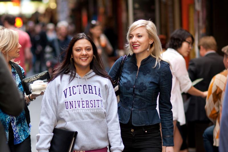 Two students standing in one of Melbourne's busy laneways. One of the students is wearing a Victoria University sweater.