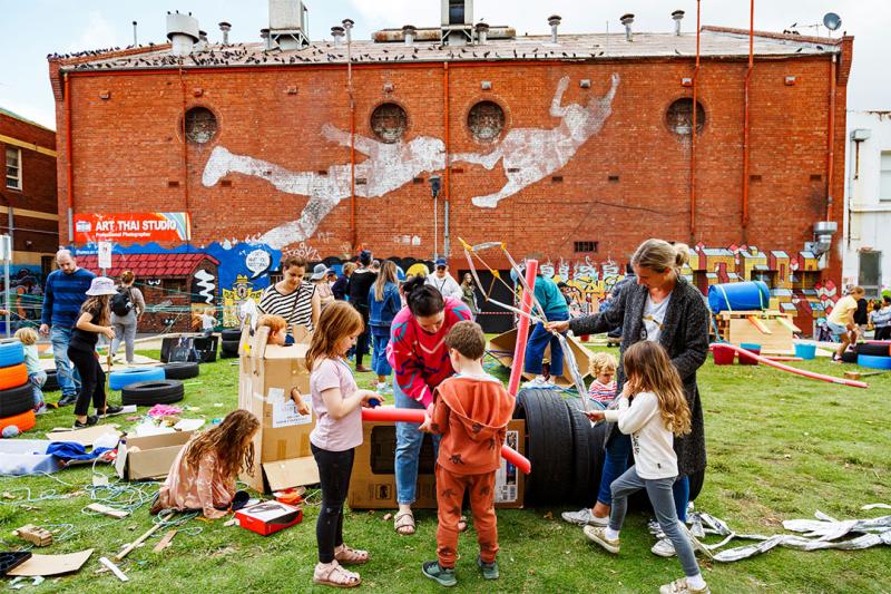 A group of kids and Early Childhood teachers gather on the grass in Footscray, engaged in tasks. Image credit: Gianna Rizzo.